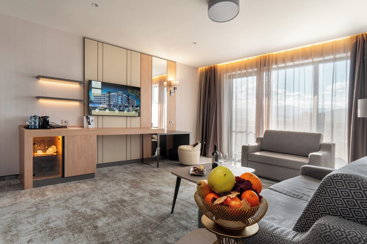 A modern living room with a sofa, a coffee table, a fruit bowl, and a television mounted on the wall.