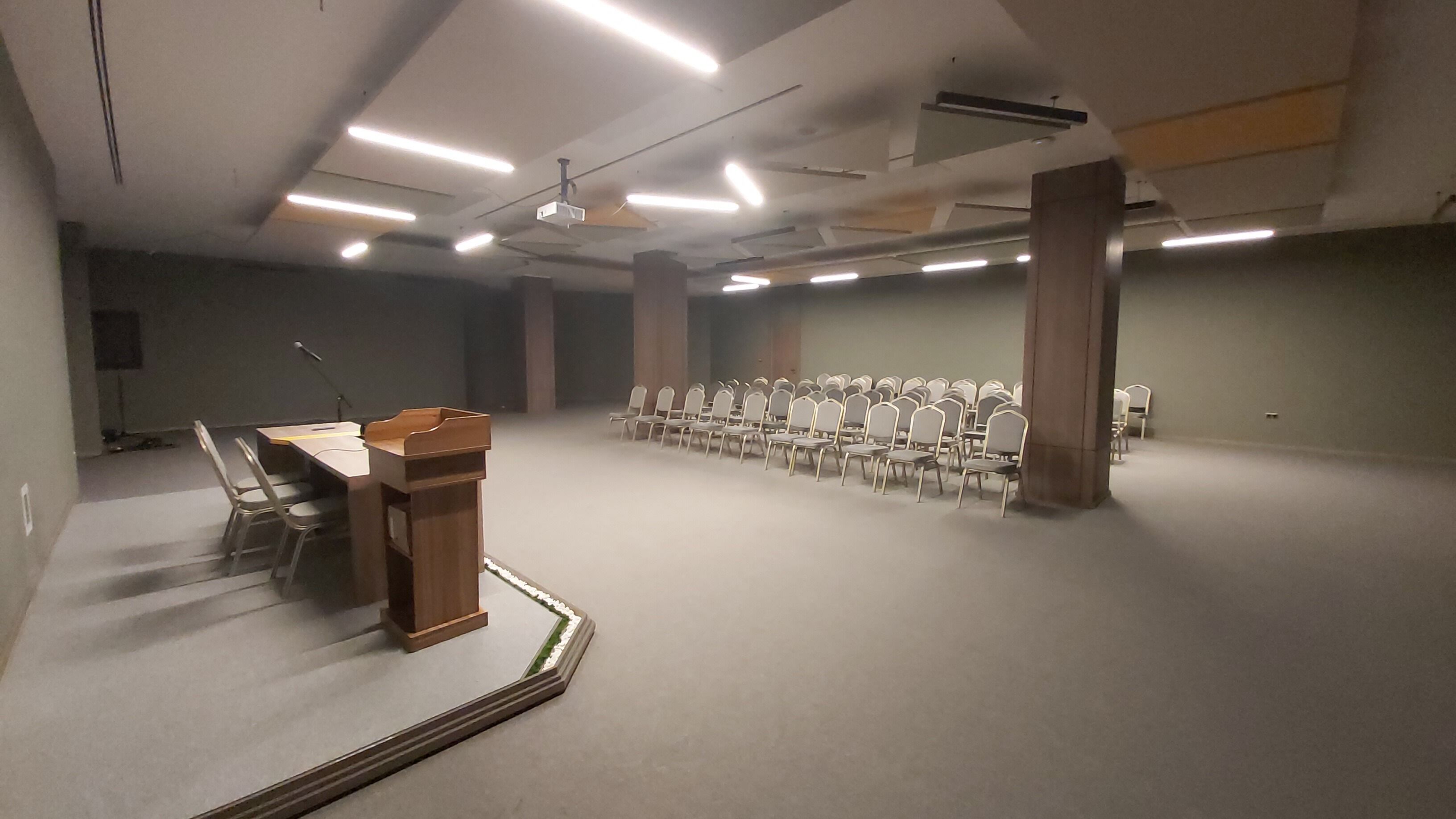 A conference room with a podium, rows of chairs, and ceiling lights.