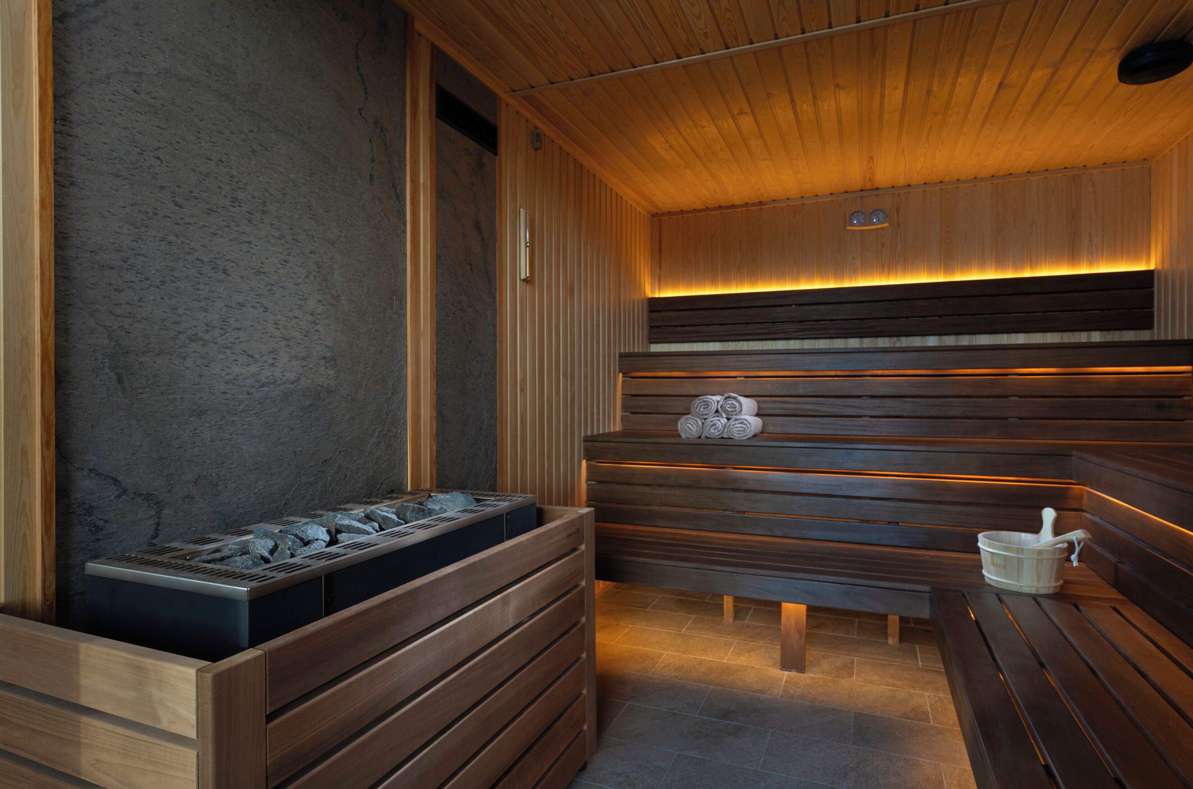 A sauna with wooden benches and a stone bench, a stone bench with a bucket, and a stone bench with a towel holder.