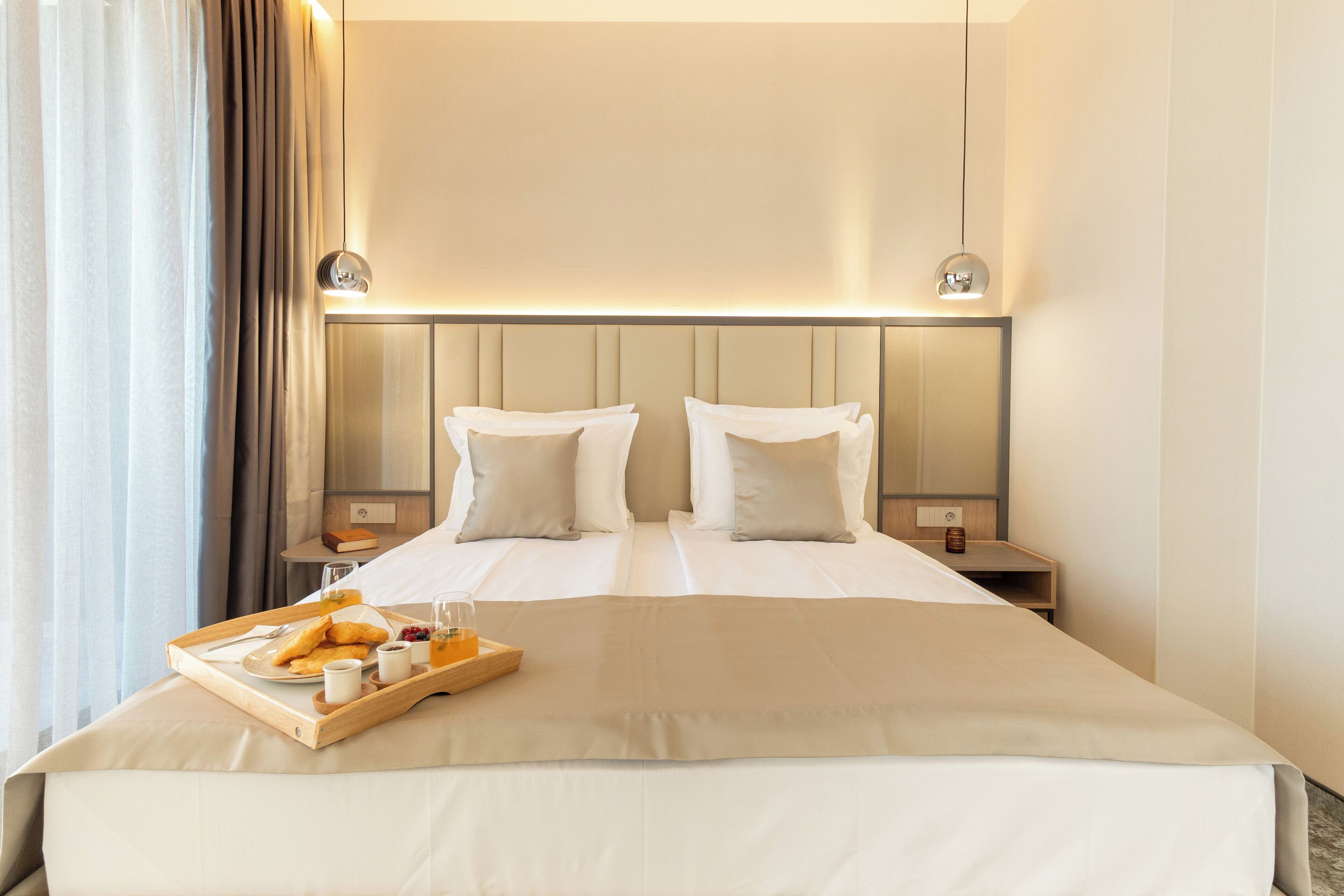 Een hotelkamer met een groot bed, twee nachtkastjes, een dienblad met ontbijtartikelen en een hoofdeinde met ingebouwde verlichting.