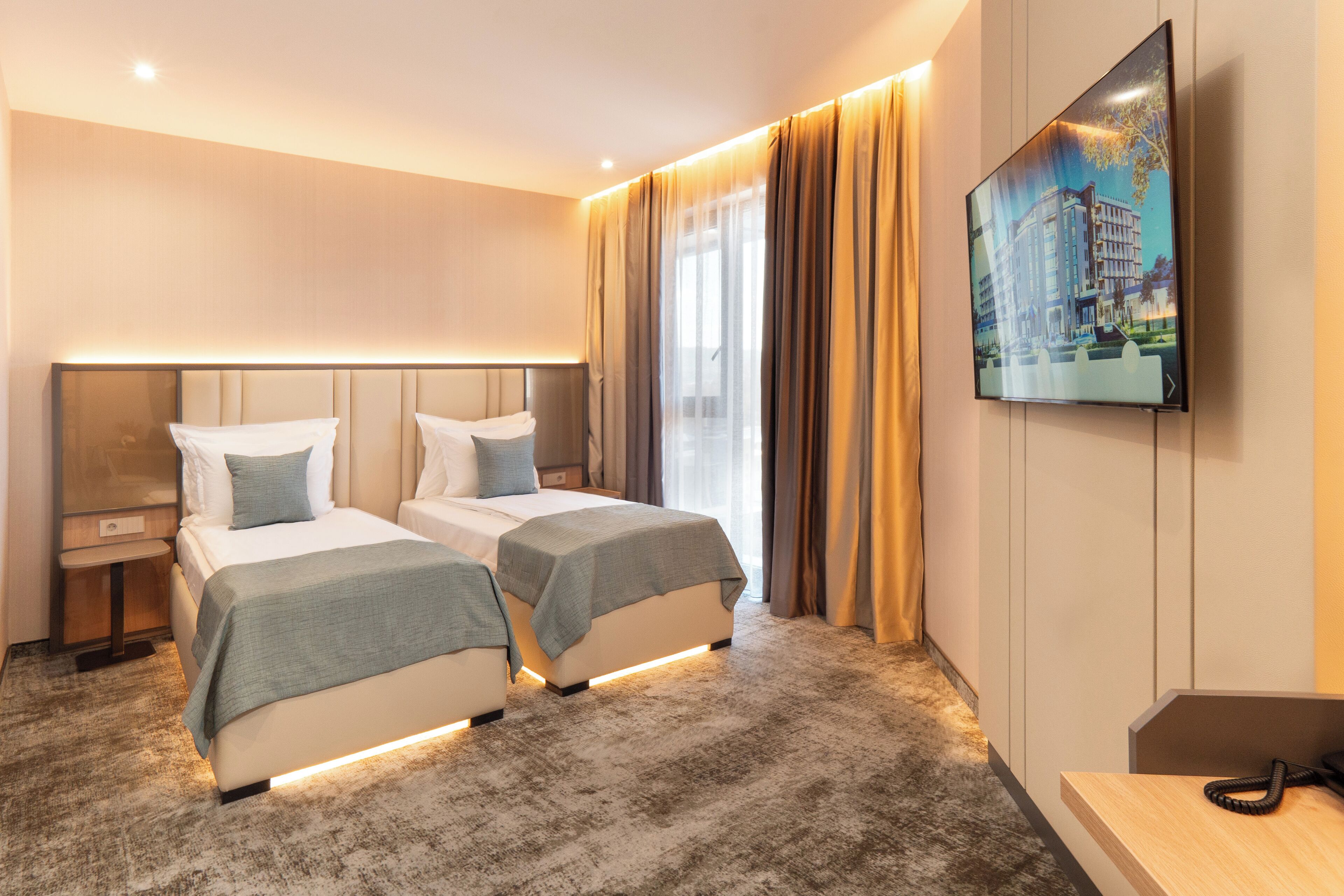 Ein Hotelzimmer mit zwei Betten, einem an der Wand befestigten Fernseher und einem Schreibtisch mit Telefon.