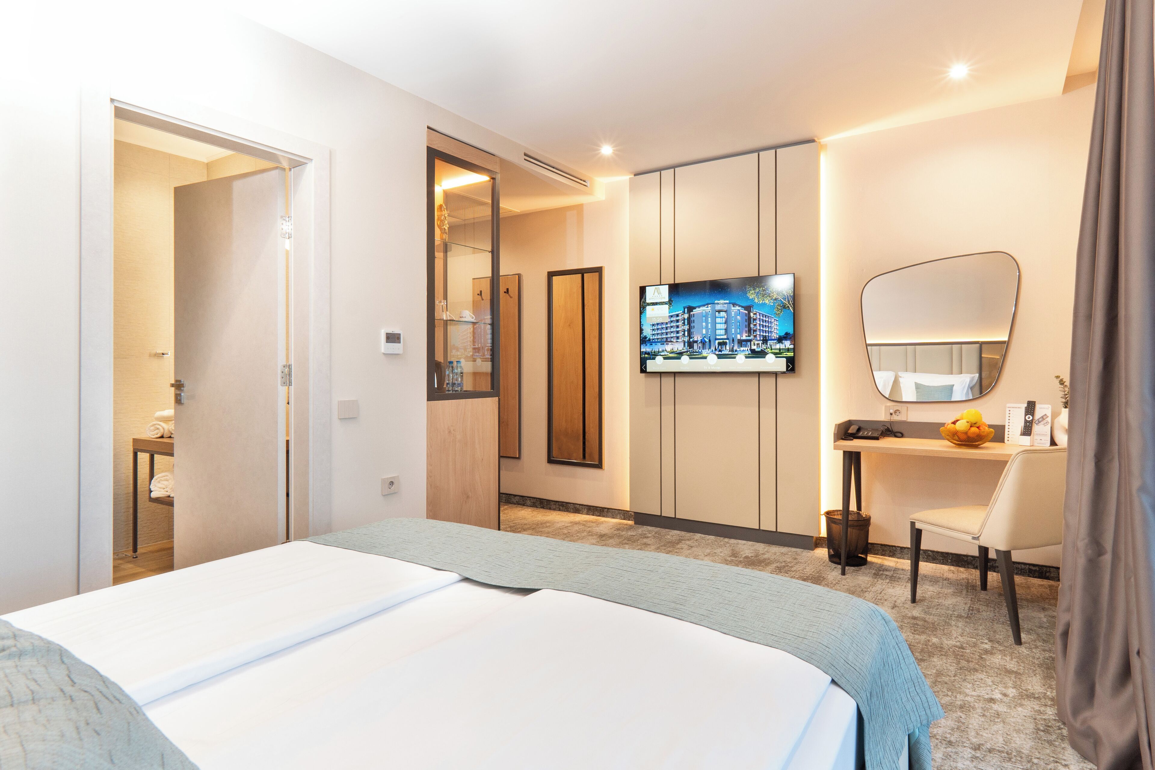 Habitación de hotel con cama, escritorio, silla, televisor y espejo.