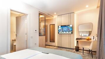 Habitación de hotel con cama, escritorio, silla, televisor y espejo.