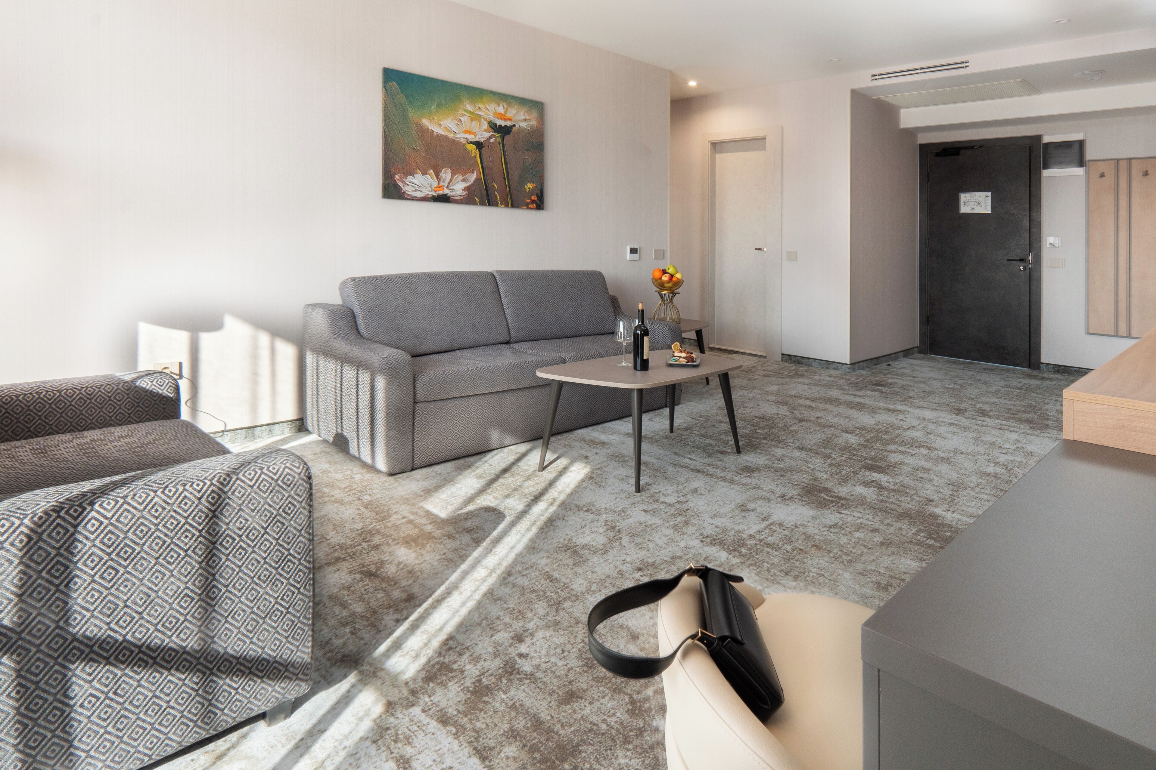 A modern living room with a grey sofa, a coffee table with a vase of flowers, and a painting on the wall.
