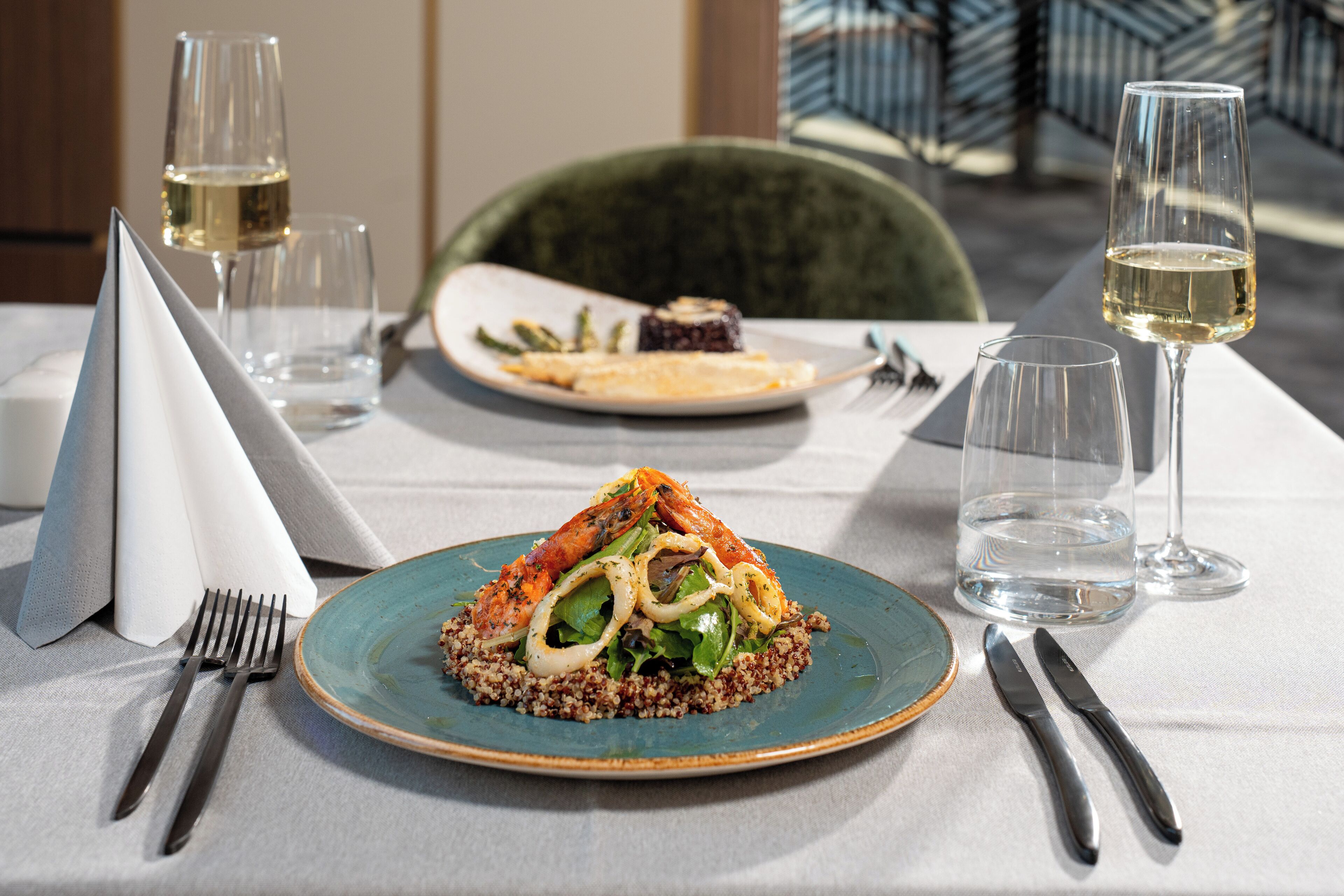A dining table with a plate of food, a glass of wine, and cutlery.