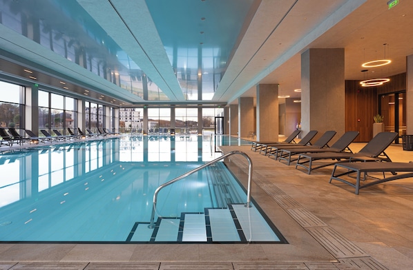 Una piscina interior con tumbonas y una vista despejada del paisaje urbano a través de amplias ventanas.