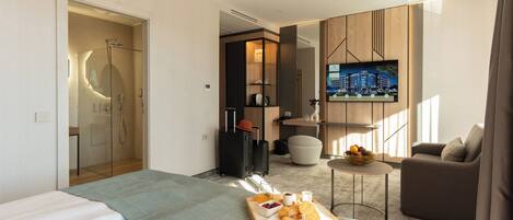 Una habitación de hotel moderna con una cama grande, una zona de estar con televisor y una pequeña mesa con productos para el desayuno.