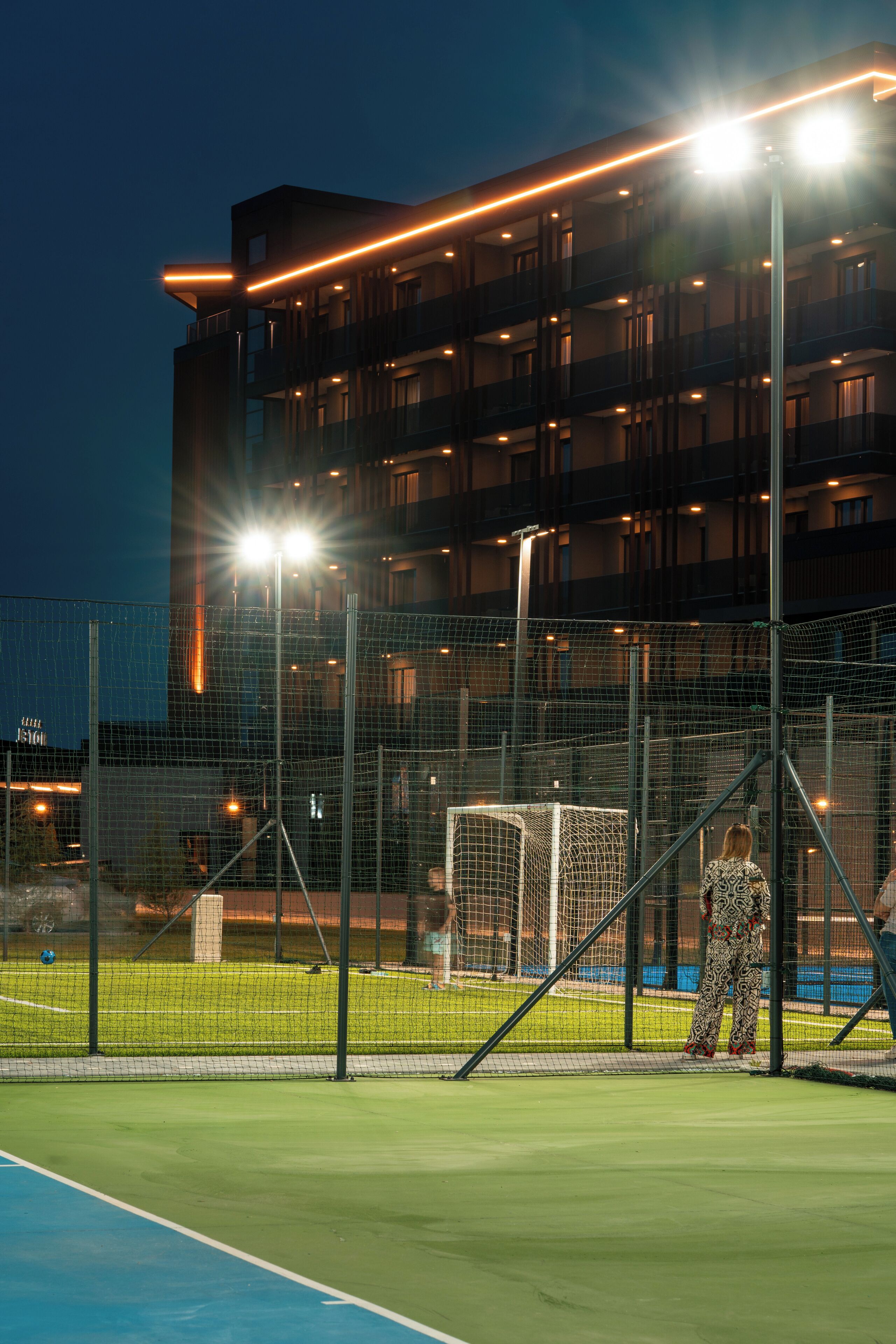A sports court with a netted fence, a goalpost, and a building with multiple balconies in the background.