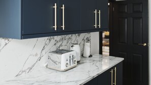 Une cuisine avec des meubles de couleur sombre, un plan de travail en marbre et un grille-pain blanc.
