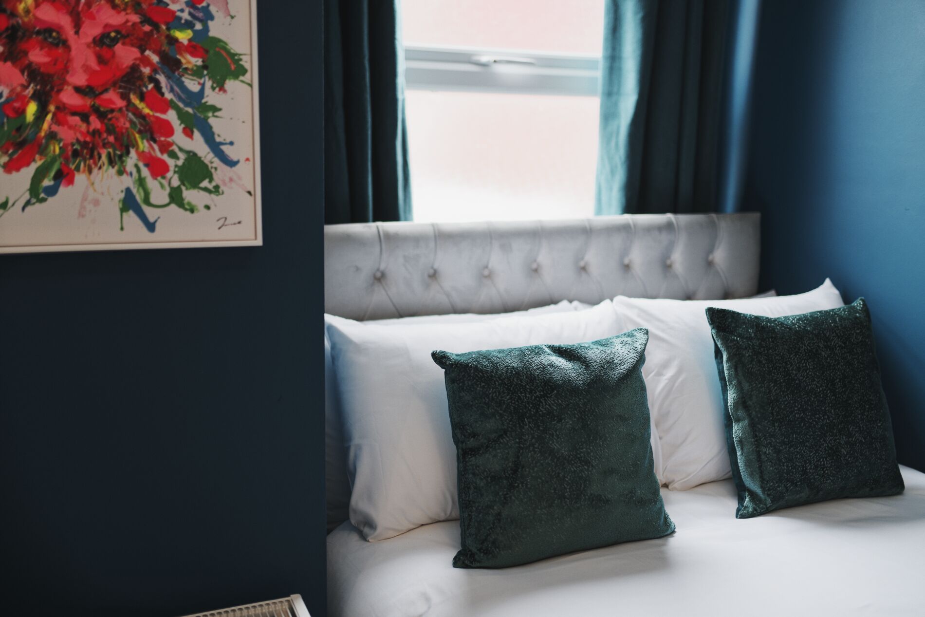 Un dormitorio con cabecera capitonada, ropa de cama blanca y dos almohadas verde oscuro.