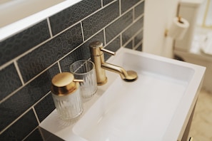 A bathroom sink with a gold faucet, a glass with a gold lid, and a black and white patterned tile backsplash. - Captivating 2-bed Apartment in Liverpool (Liverpool)