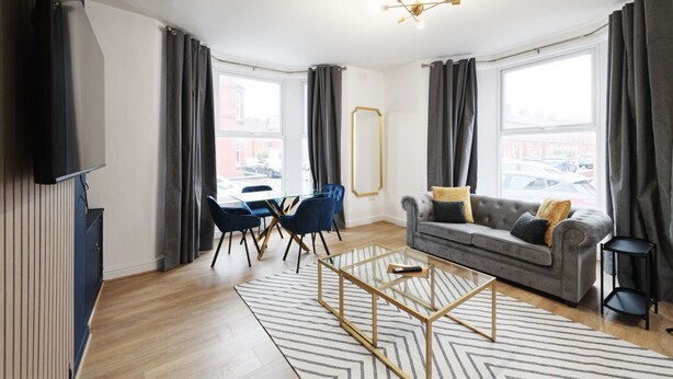 Un salon moderne avec un canapé, une table basse en verre, un téléviseur et une grande fenêtre avec des rideaux.
