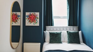 Une chambre à coucher avec un lit, deux tableaux, un miroir et une fenêtre avec des rideaux.
