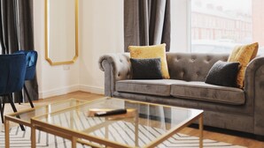 Un salon moderne avec un canapé gris, deux coussins, une table basse en verre et une chaise bleue.
