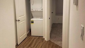 Une buanderie équipée d’un lave-linge et d’un sèche-linge, avec un sol recouvert de moquette et une porte donnant sur une autre pièce.