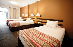 Habitación de hotel con tres camas, cada una con una colcha estampada, una mesita de noche con lámpara y teléfono.