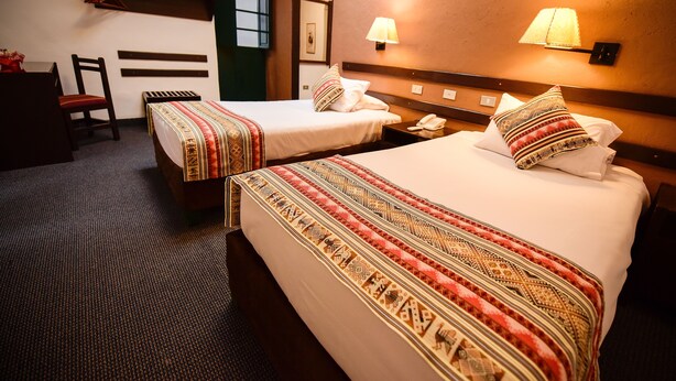 Une chambre d’hôtel avec deux lits, un bureau, une chaise et une lampe.