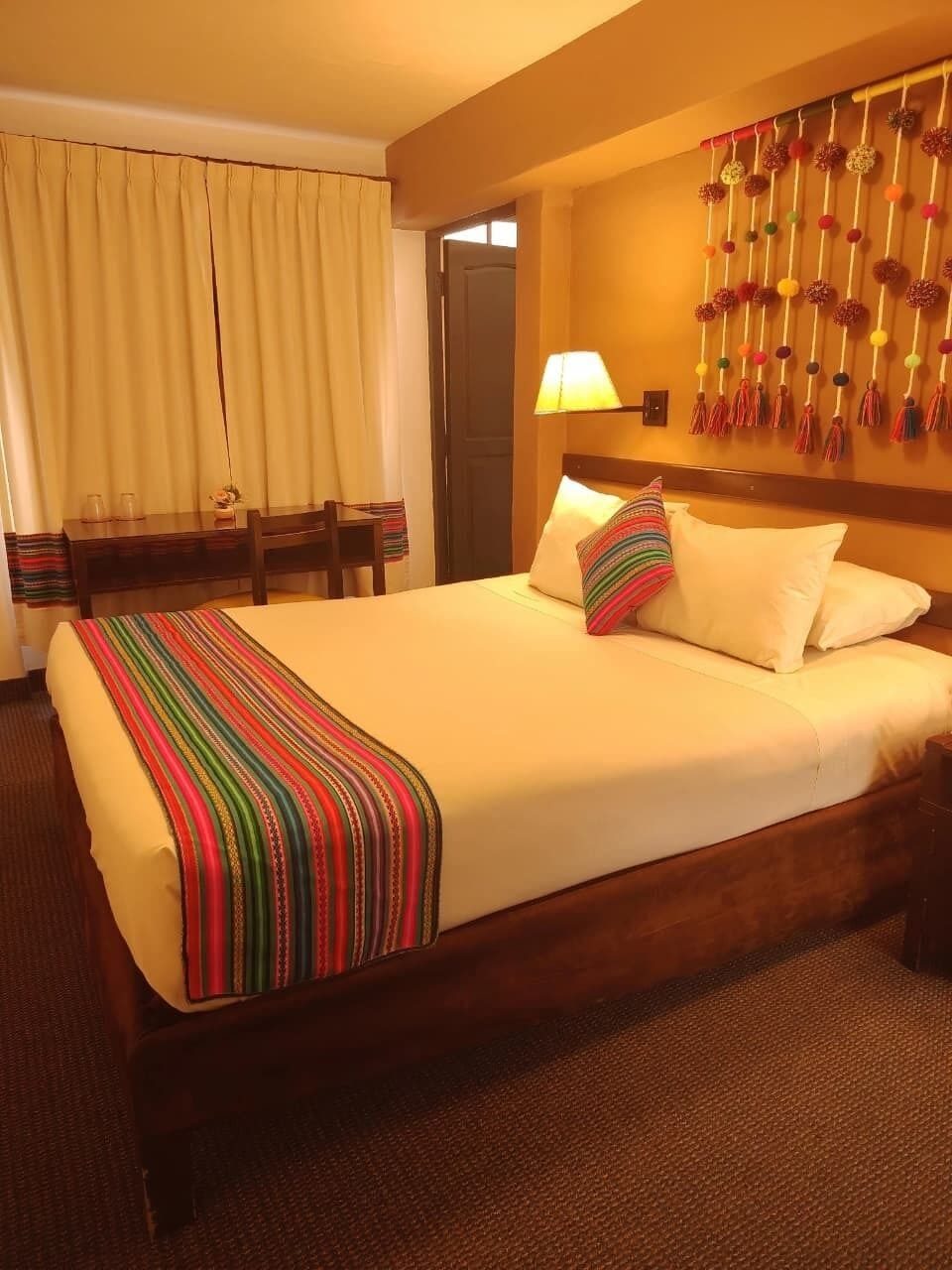 A hotel room with a large bed, a desk with chairs, a lamp, and a wall decoration.