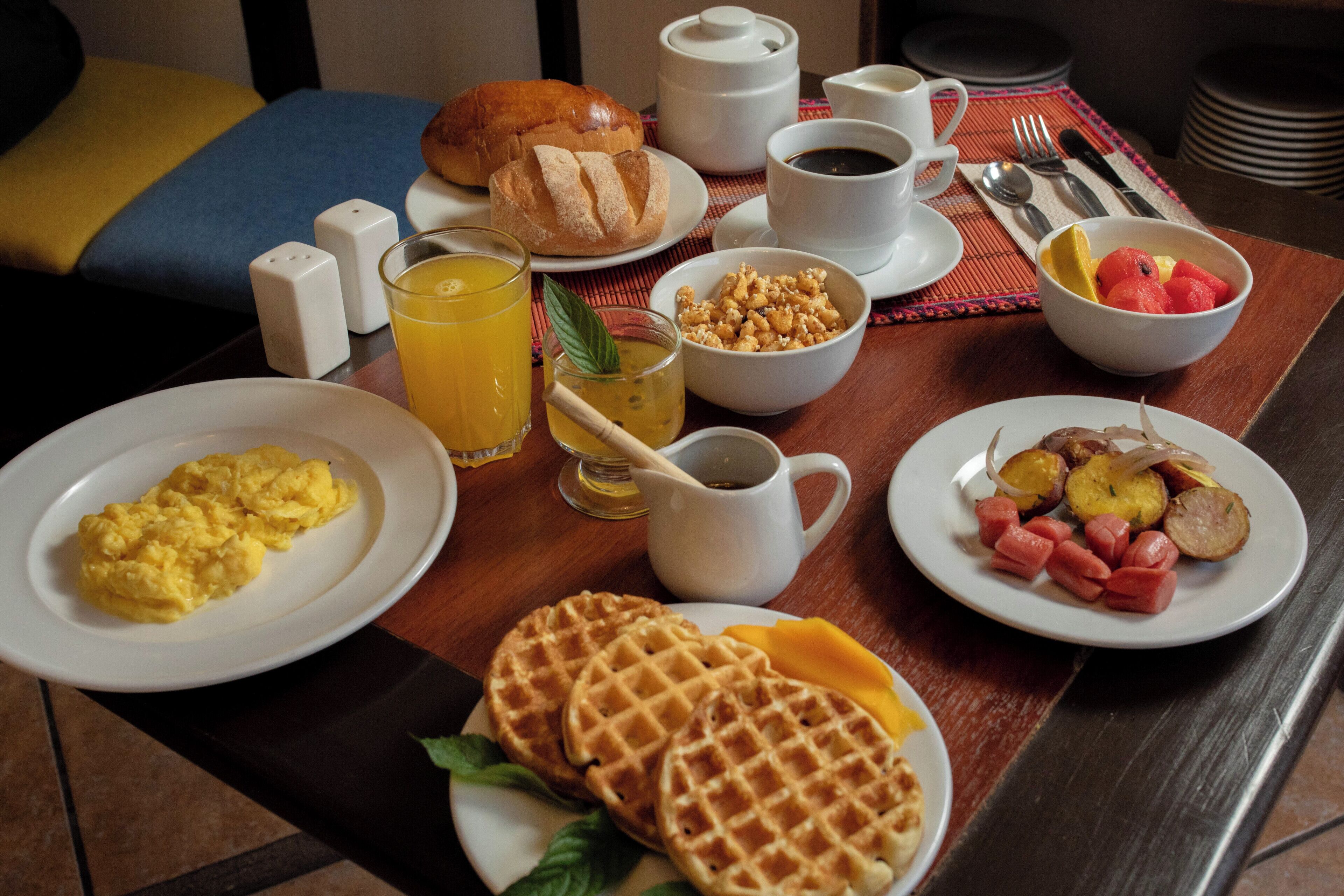 Une table de petit-déjeuner avec des assiettes contenant des œufs brouillés, des gaufres et des fruits.