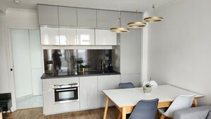 A modern kitchen with white cabinets, a black countertop, and a built-in oven. There is a dining table with chairs and a potted plant. - Sublime Appartement Proche de Paris et La Défense Arena (Courbevoie)