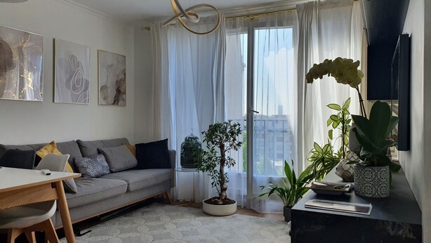 A modern living room with a sofa, a dining table, and a potted plant. - Sublime Appartement Proche de Paris et La Défense Arena (Courbevoie)