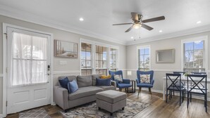 A spacious living room with a grey sectional sofa, blue armchairs, a dining table with chairs, and a ceiling fan. - The Wave @ Coastal Retreat Villas (Long Beach)