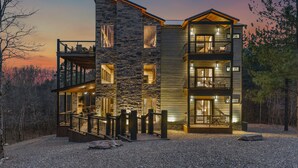 Een modern huis met meerdere verdiepingen, een gevel van natuursteen, diverse balkons en een grindpad.