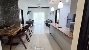 A modern kitchen with a long wooden dining table, a built-in island, and pendant lighting.