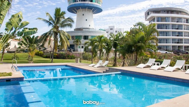 A swimming pool with lounge chairs, palm trees, and a lighthouse in the background.