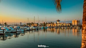 A marina with boats docked, a lighthouse, and buildings in the background.