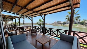 Un espacio de estar al aire libre techado, con mobiliario de madera y vistas al agua.