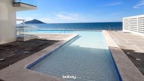 En swimmingpool med udsigt til havet og et bjerg, omgivet af moderne bygninger.
