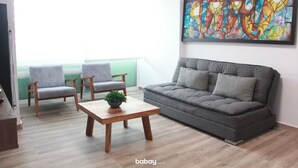 En moderne stue med en grå sofa, to grå lænestole, et træ sofabord med en plante og et farverigt abstrakt maleri på væggen.