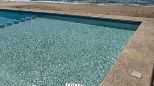 Klar blå himmel, en swimmingpool og en strand med en fjerntliggende ø.