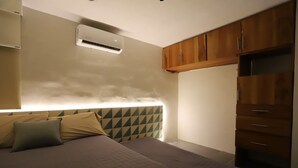 A bedroom with a bed, a headboard with a geometric pattern, a wardrobe, and an air conditioning unit.