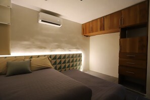 A bedroom with a bed, a headboard with a geometric pattern, a wardrobe, and an air conditioning unit.
