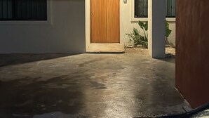 A modern building entrance with a wooden door, a concrete floor, and a small window to the right.