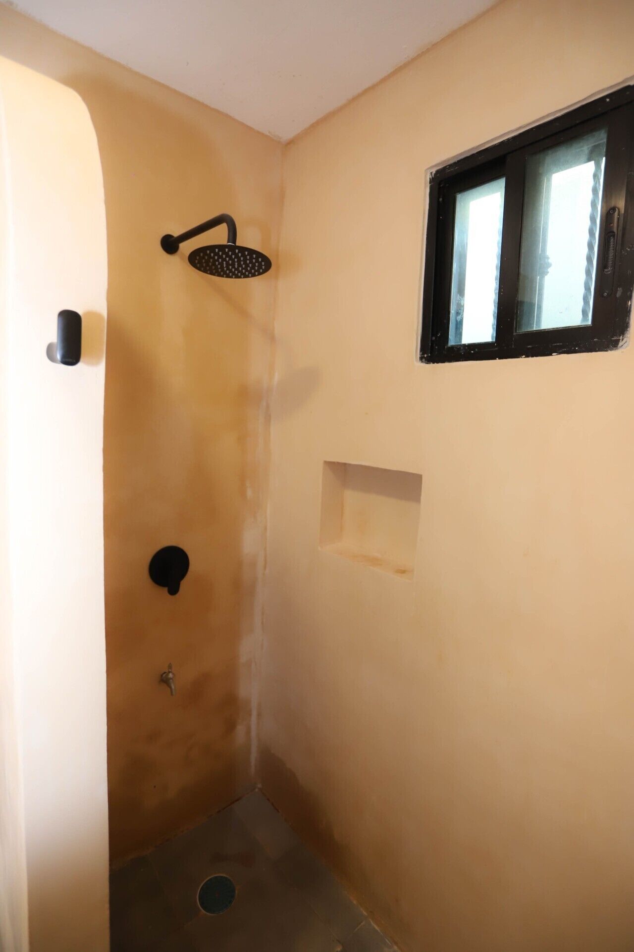 A small, enclosed shower area with a handheld showerhead, a window, and a small shelf.