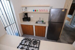 Een kleine keuken met een gasfornuis, een koelkast, een koffiezetapparaat en een spoelbak.