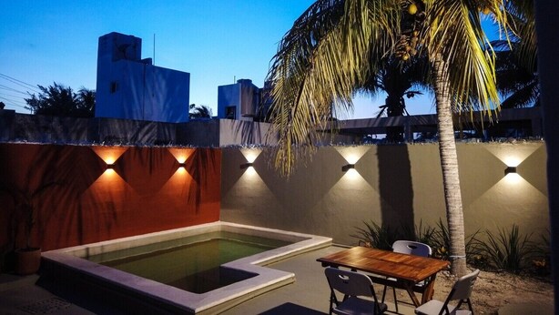 Una piscina con muelle de madera, una mesa y sillas, rodeada por un muro bajo con luces empotradas.