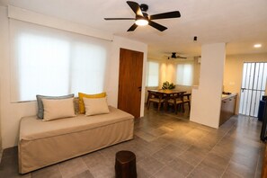 A living room with a sofa, a dining table, and a kitchen area.