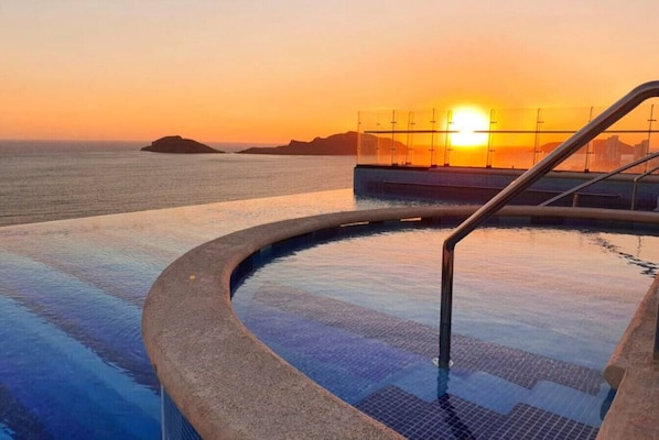 A swimming pool with a view of the sunset over the ocean.