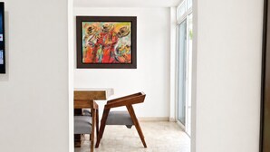 Un pasillo interior con pared blanca, un cuadro enmarcado, una mesa de comedor de madera con sillas y piso de baldosas.