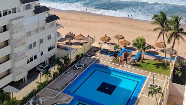 Un hotel con piscina, vista al mar y palmeras.