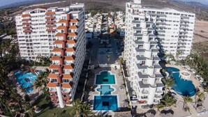 Un hotel de altura con varios balcones, una piscina central y vista a la playa.