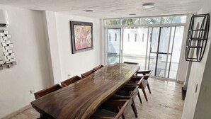 Una habitación amplia con una larga mesa de madera y sillas, un cuadro enmarcado en la pared, y un gran ventanal que ofrece vistas al exterior.