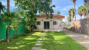 A single-story house with a tiled roof, a stone wall, and a paved driveway leading to the entrance. - Altata, casa Las Aguilas (Altata)