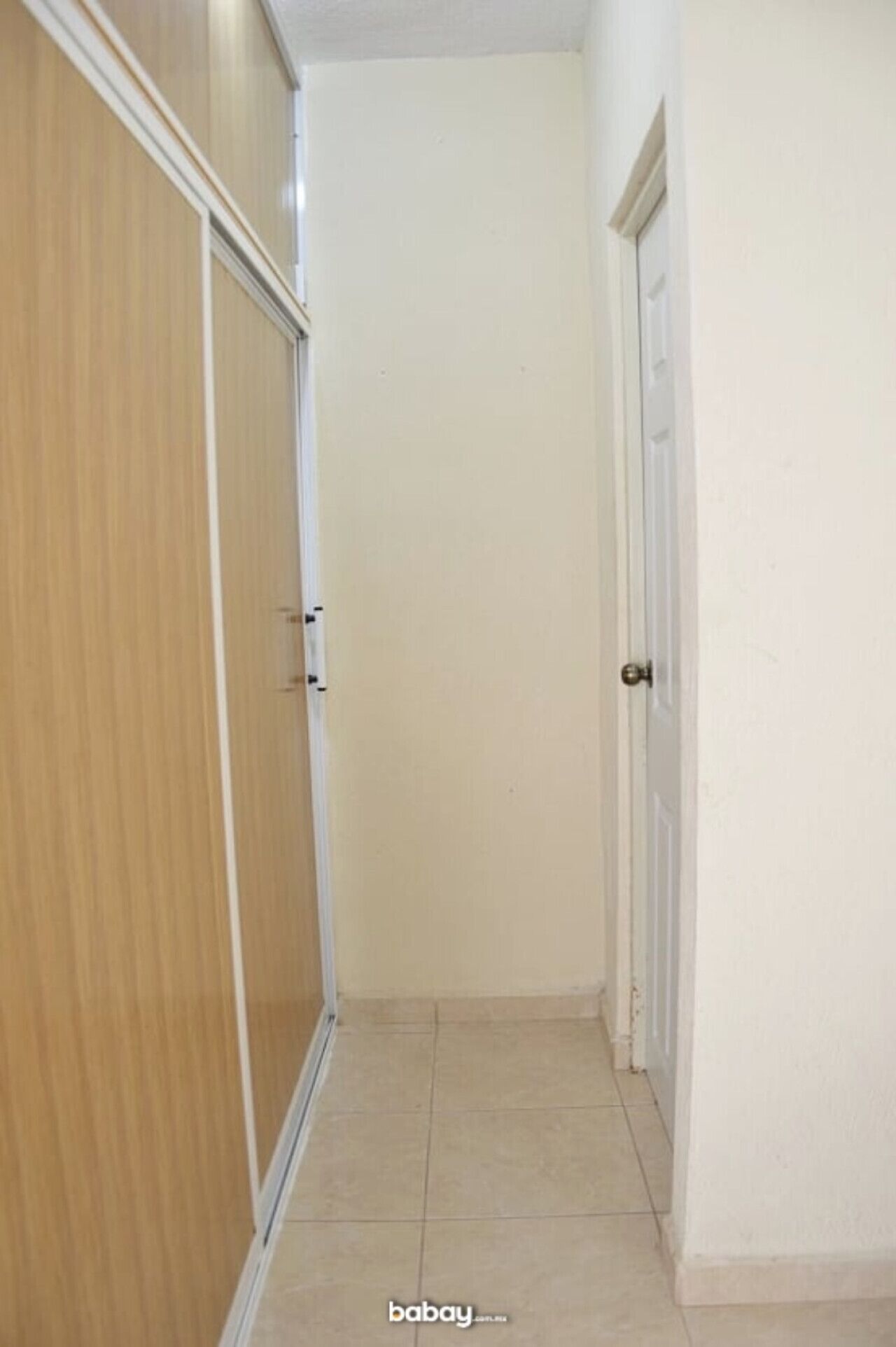 Un couloir étroit, avec une armoire en bois sur la gauche et une porte blanche sur la droite.