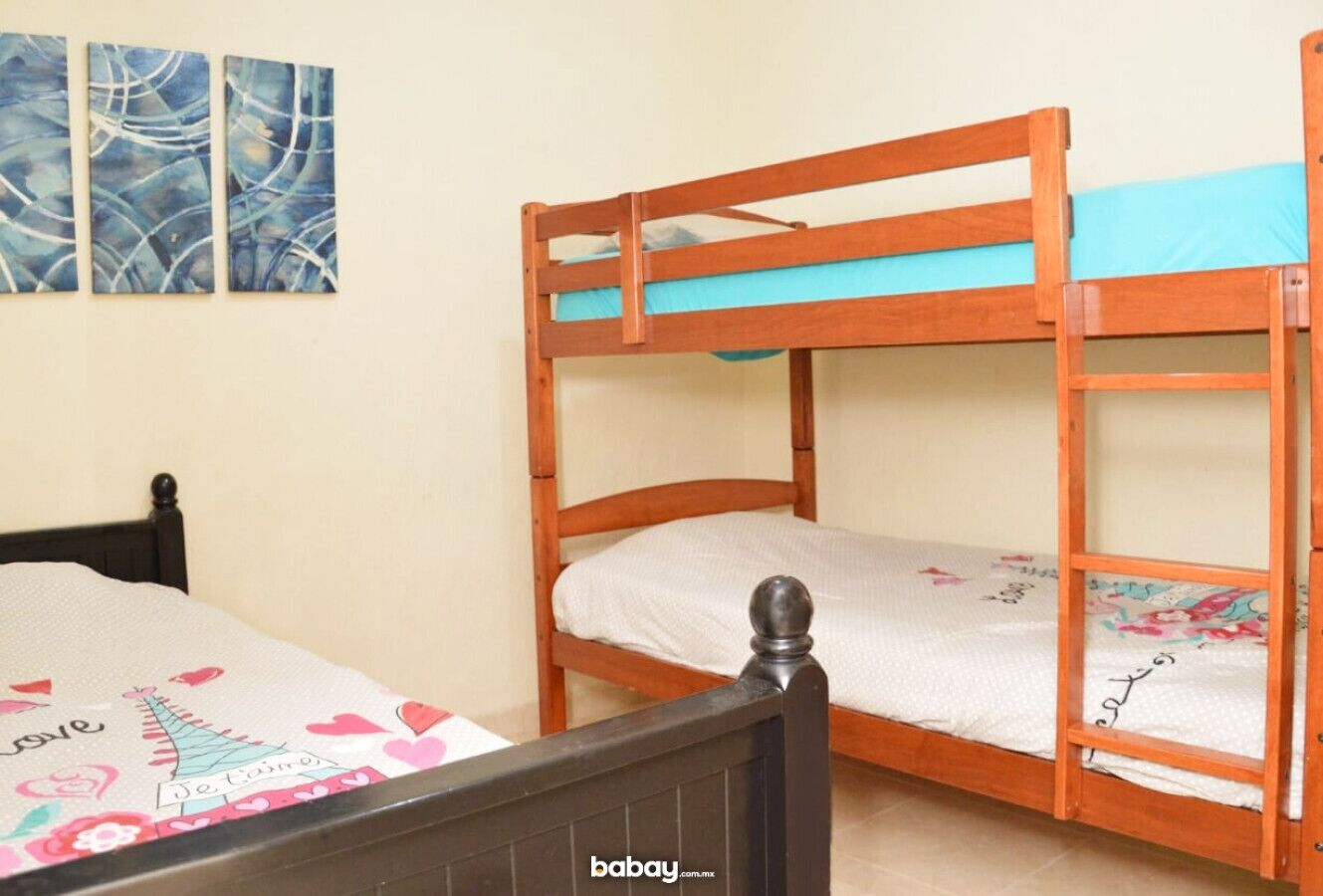 A bunk bed with a wooden frame and a lower bed with a white sheet. There is a blue wall art piece above the bed.