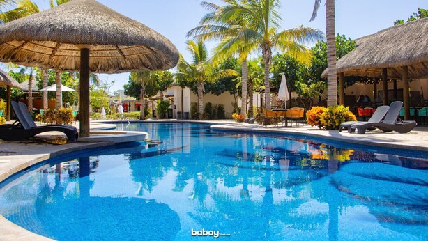 A swimming pool with lounge chairs and thatched umbrellas, surrounded by palm trees and greenery. - Casa en nuevo Altata, Punta Esmeralda Grand (Nuevo Altata)